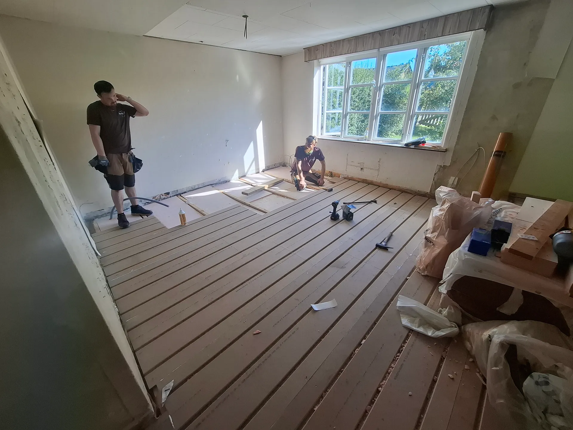 To tømrere fra Broe Byggeservice lægger strøer i et rum under renovering